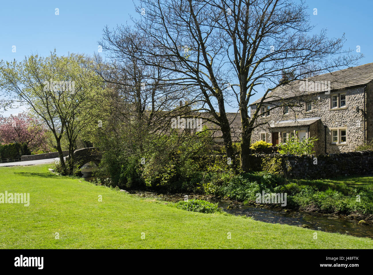 Cottage in pietra affacciato sul verde del villaggio e Malham Beck in Malham, Malhamdale, Yorkshire Dales National Park, North Yorkshire, Inghilterra, Regno Unito, Gran Bretagna Foto Stock