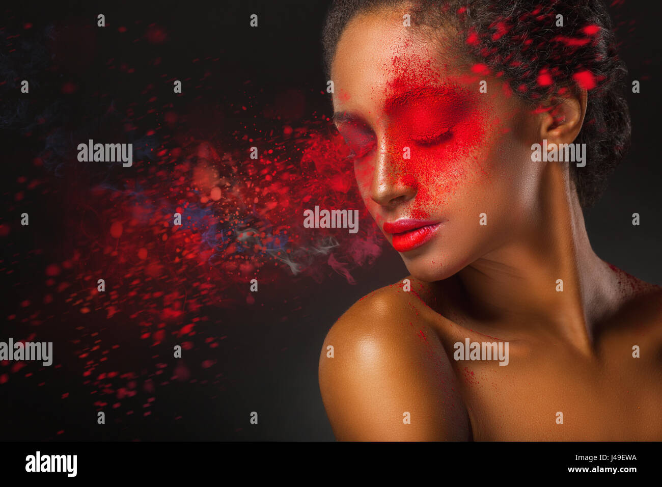 Il trucco di moda. Close-up volto di una giovane e bella donna con spruzzi di vernice rossa su uno sfondo nero Foto Stock