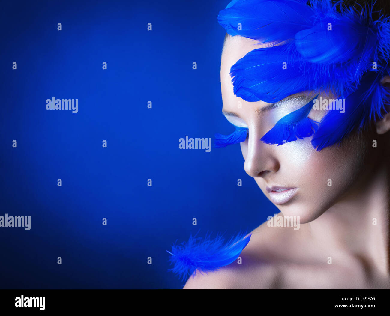 Attraente giovane donna con il make-up con blu brillante piume su uno sfondo blu Foto Stock