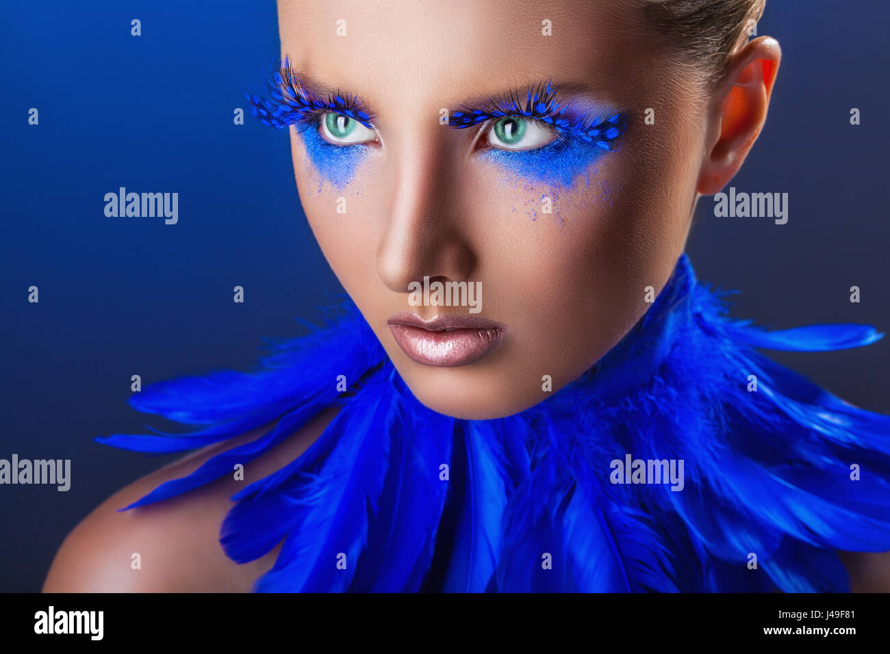 Attraente giovane donna con il make-up con blu brillante piume su uno sfondo blu Foto Stock