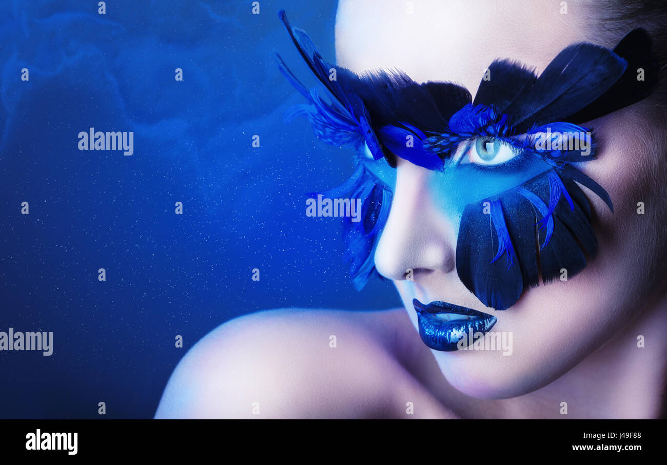 Bella donna con il make-up con piume blu su sfondo blu Foto Stock