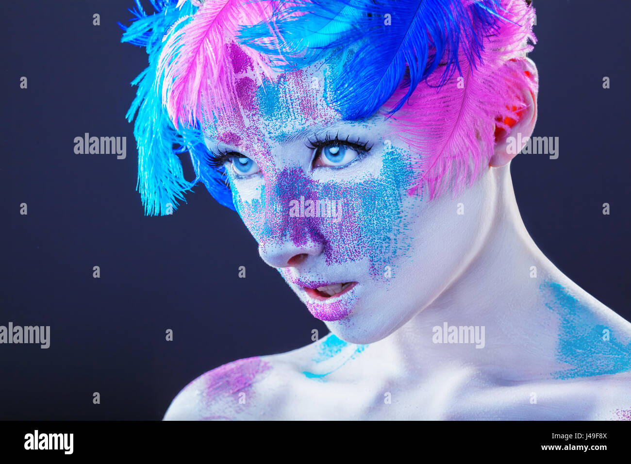 Un attraente giovane donna con il make-up con luminosi piume colorate su sfondo scuro Foto Stock