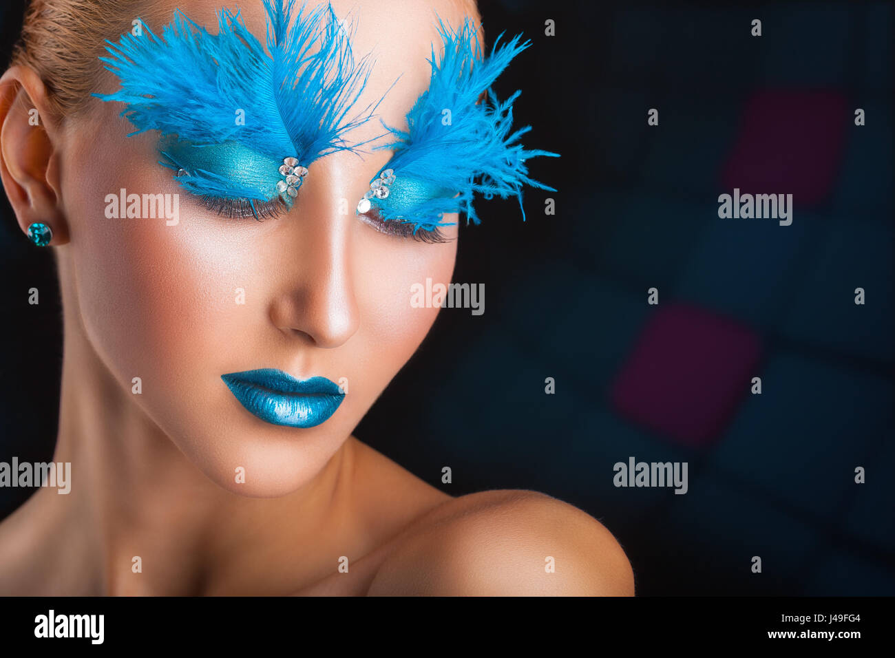 Donna attraente con brillante trucco con piume blu su sfondo scuro Foto Stock