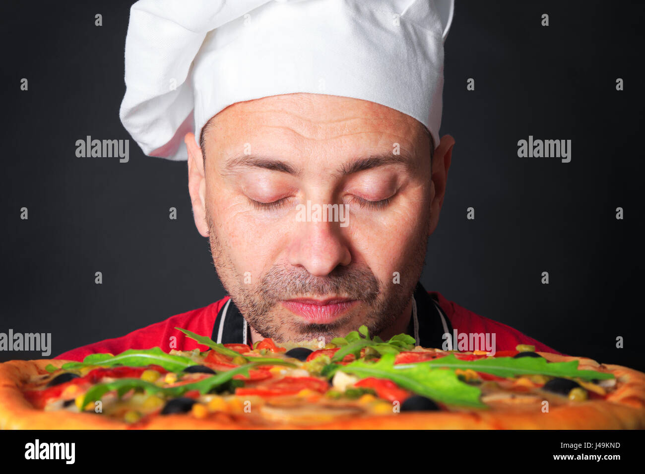 Ritratto di felice attraente cook con una pizza in studio un sfondo nero Foto Stock