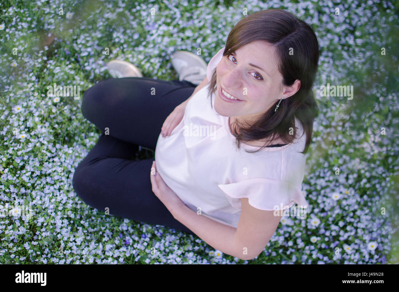 Donna incinta seduta sorridente in margherite con un top ingrandirle Foto Stock