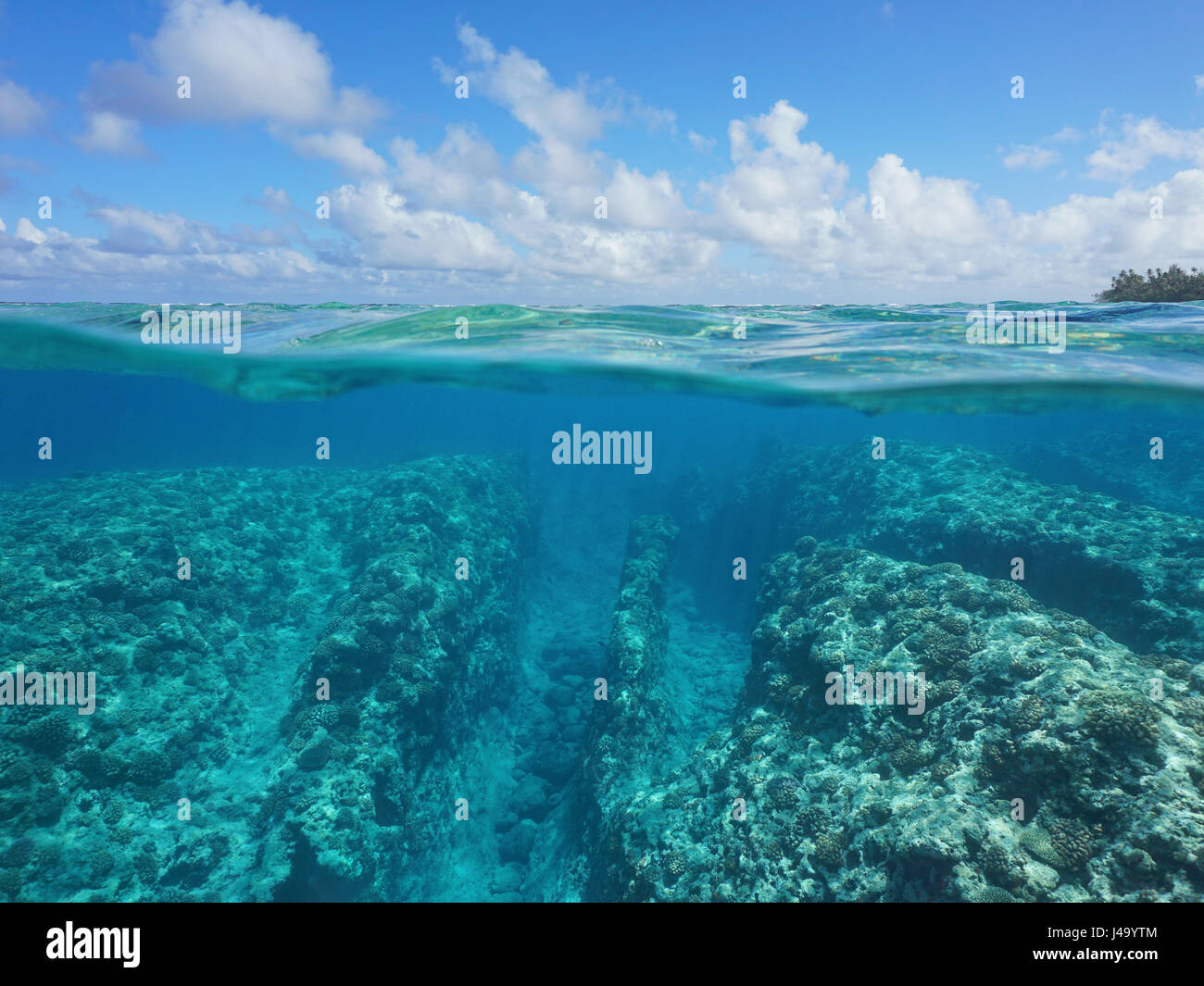 Oltre al di sotto della superficie dell'acqua, fondali rocciosi con barriera corallina subacquea e nuvoloso cielo blu divisa dalla linea di galleggiamento, Huahine, oceano pacifico, Polinesia Francese Foto Stock