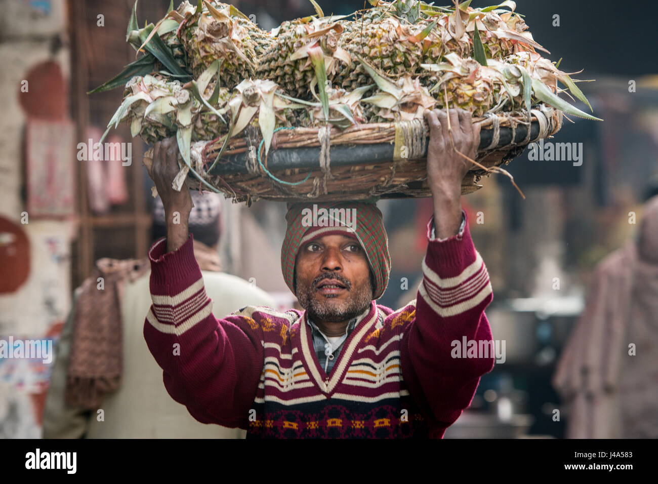 Uomo che porta gli ananassi in un grande cestino giù per una strada trafficata in New Delhi, India. Foto Stock