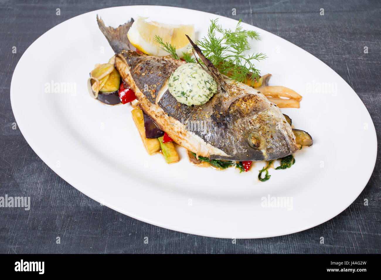 Dorado cotto con il burro e le verdure. Piastra situata su una tavola nera come sfondo. Foto Stock