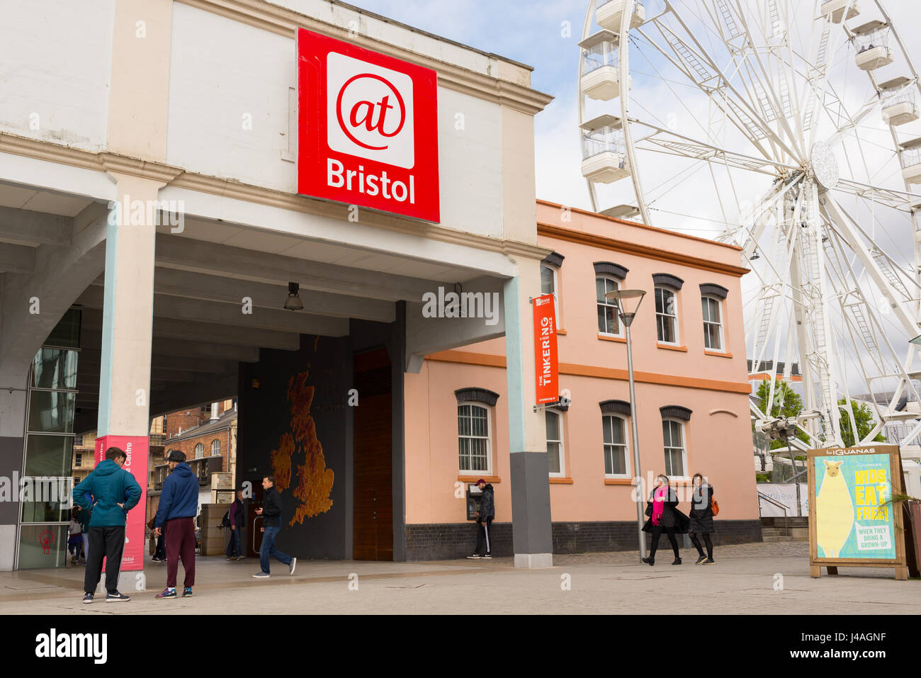 Ingresso della At-Bristol (@Bristol) museo della scienza con i visitatori e i turisti a piedi attorno a e ruota panoramica in background, Harbourside, Bristol Foto Stock
