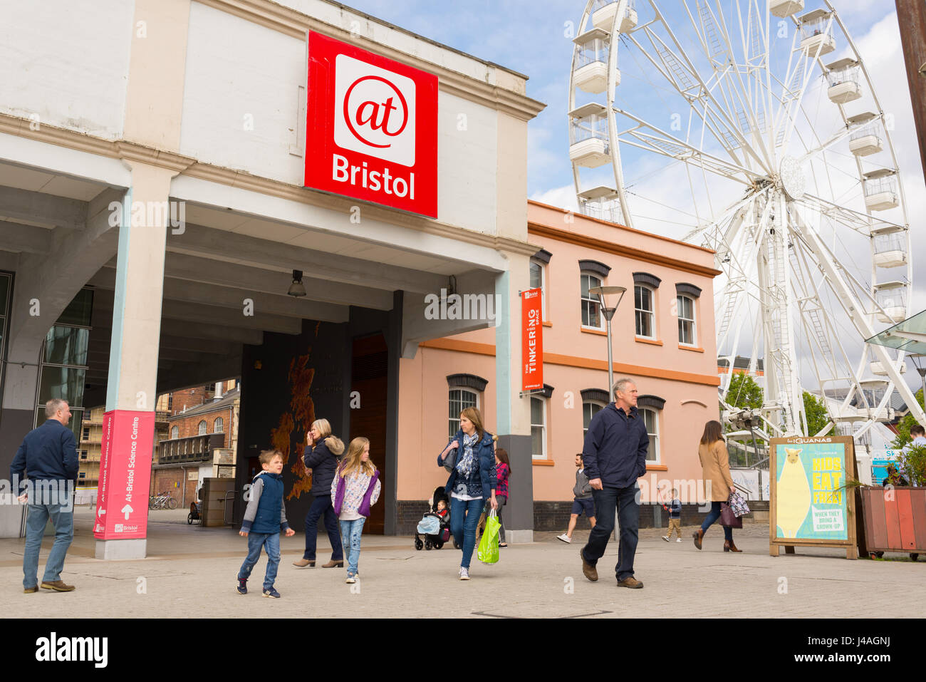 Ingresso della At-Bristol (@Bristol) museo della scienza con i visitatori e i turisti a piedi attorno a e ruota panoramica in background, Harbourside, Bristol Foto Stock