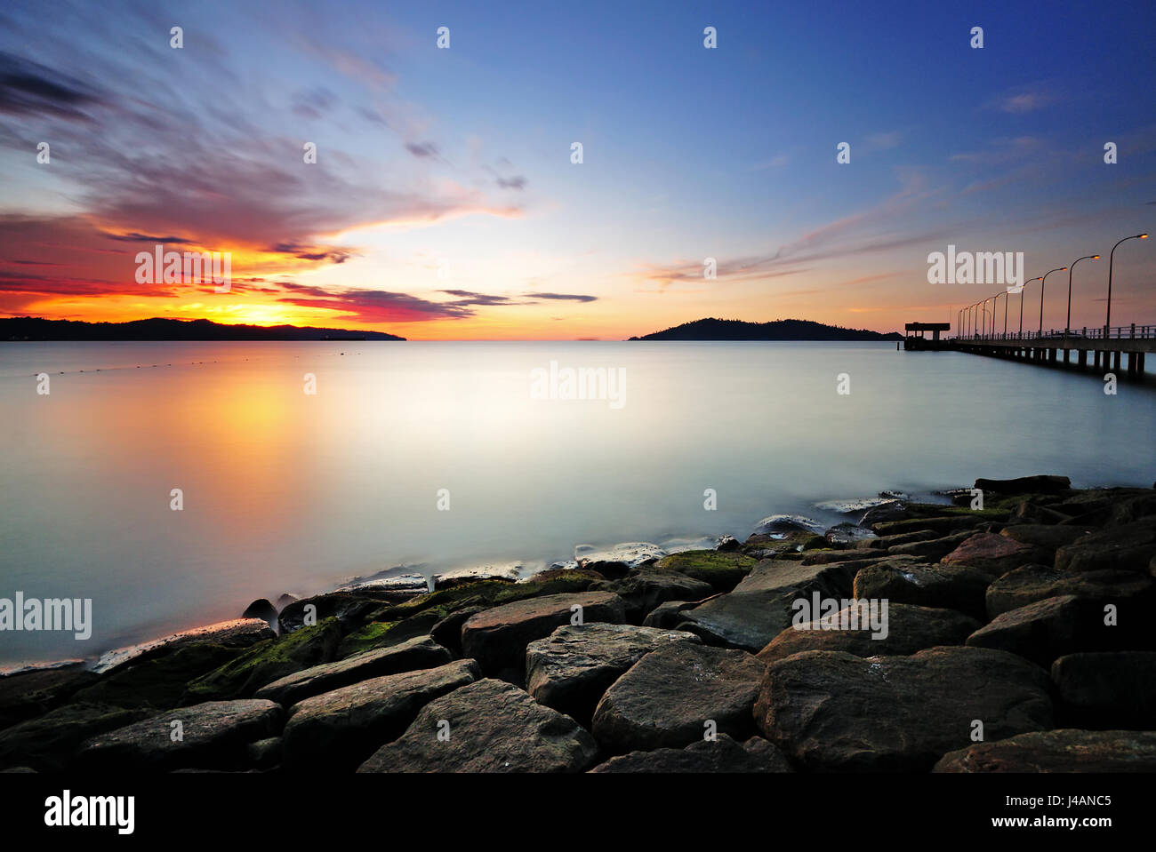 Una lunga esposizione del tramonto del sole e del mare con rocce in primo piano. Foto Stock