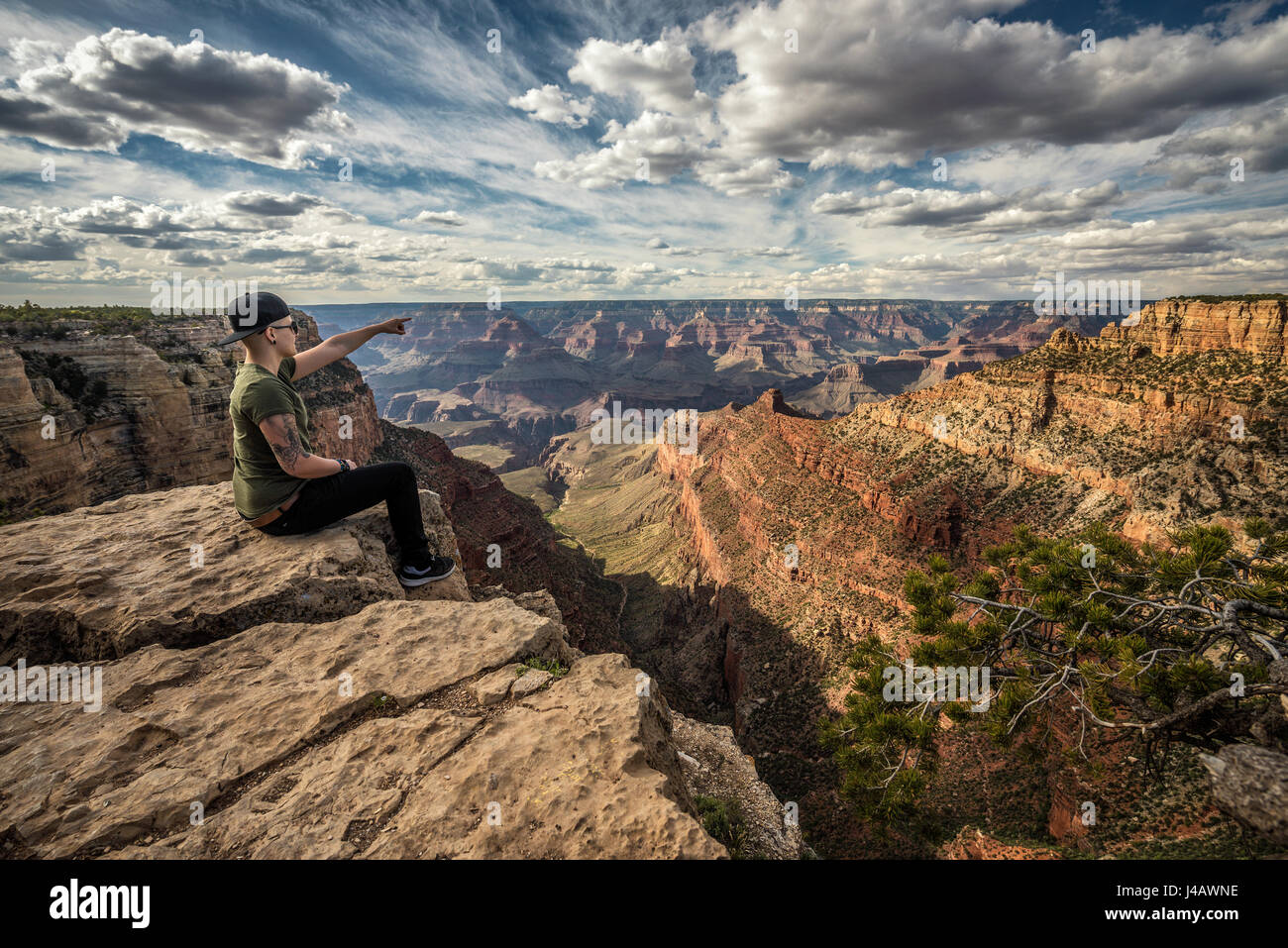 Il Grand Canyon e un giovane escursionista seduto sul bordo e a puntare a qualcosa in distanza. Foto Stock