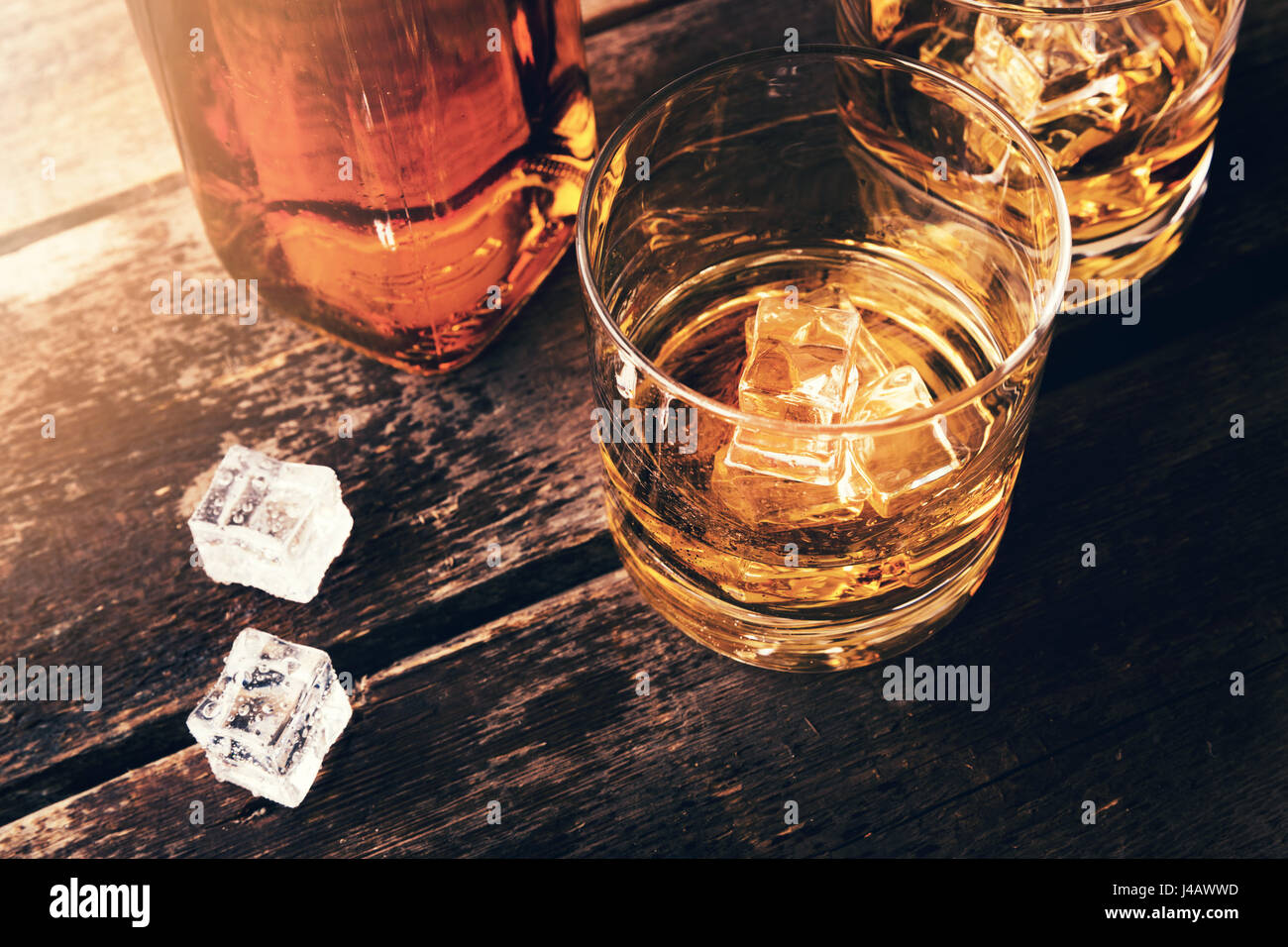 Whiskey bottiglia e bicchieri con cubetti di ghiaccio sul vecchio tavolo in legno Foto Stock