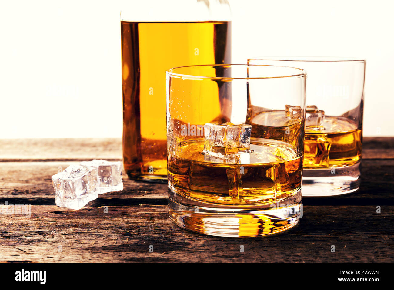 Bicchieri di whiskey e la bottiglia sul tavolo di legno contro uno sfondo bianco Foto Stock