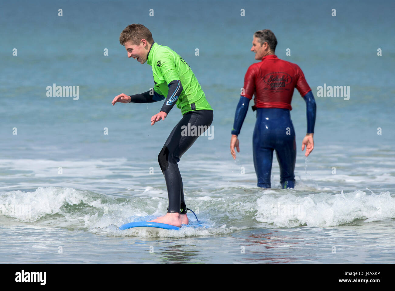 Un principiante di imparare a navigare su Fistral Beach in Newquay Cornwall fuga Scuola Surf Surf Surfers partecipanti istruttore di apprendimento aiutando Mare Foto Stock