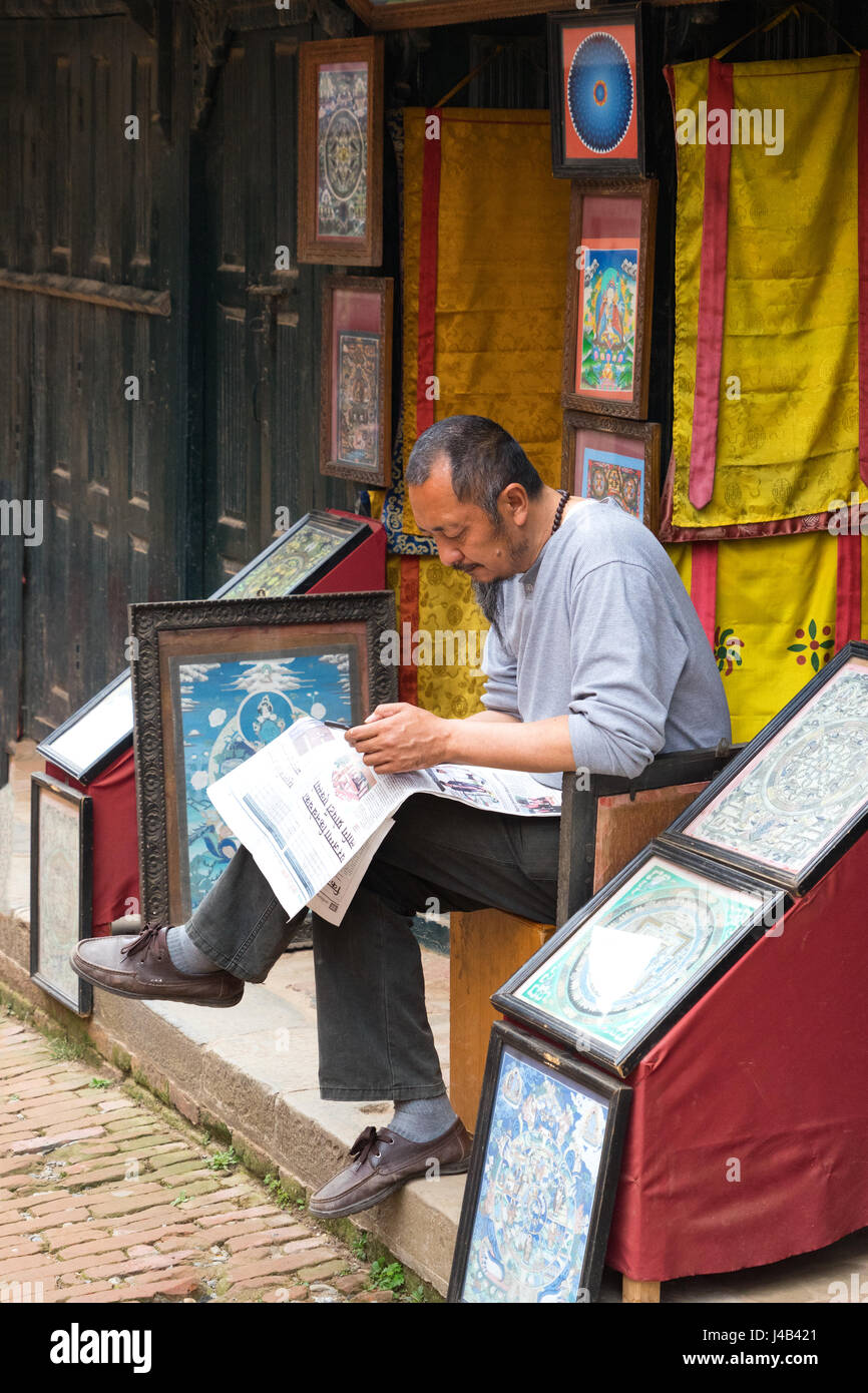 Tanka nepalese negoziante consultando il suo smartphone sul portico del suo business in Bhaktapur. Foto Stock