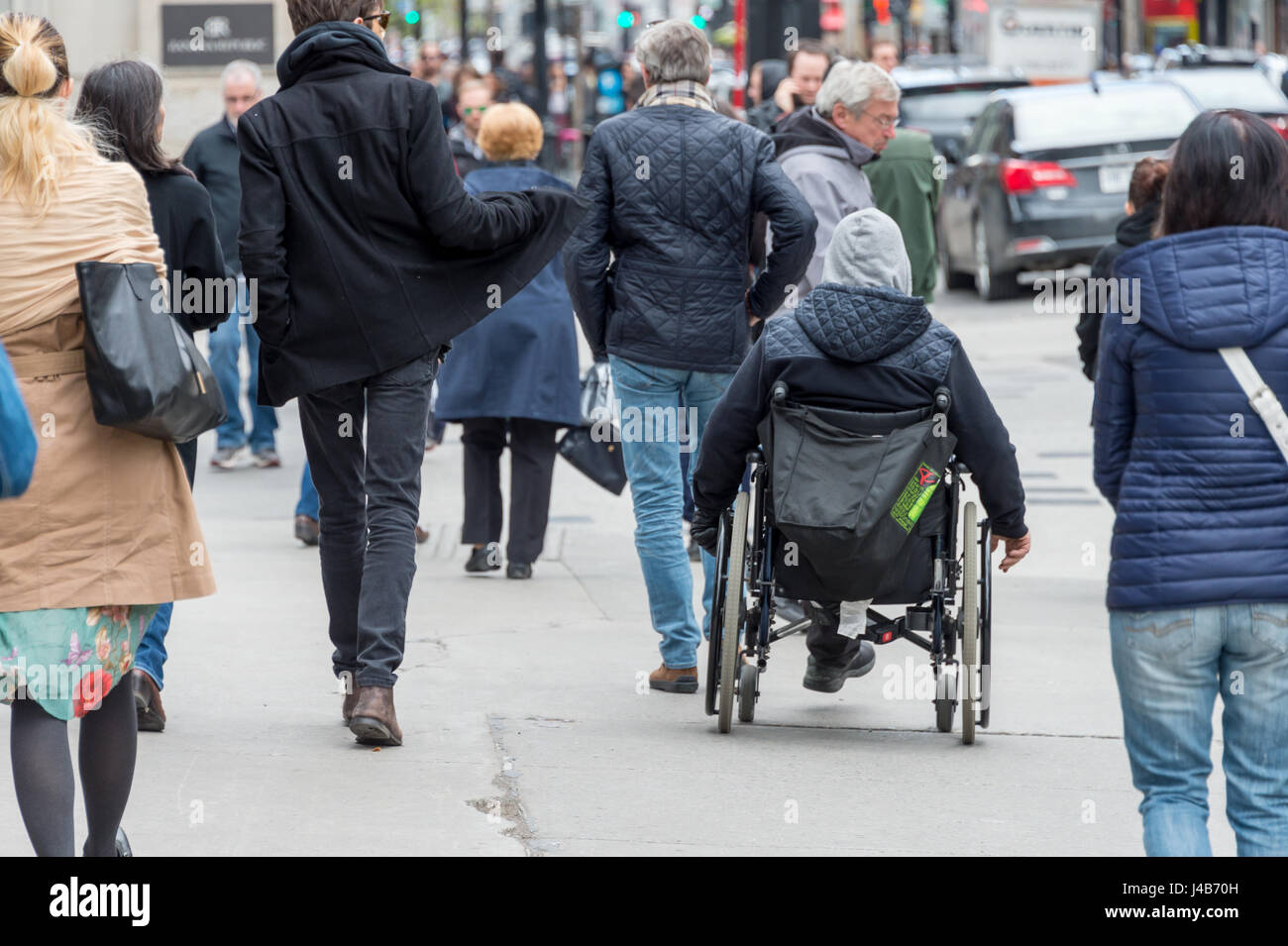 Disabilitato uomo seduto in una sedia a rotelle su una strada trafficata fra la folla di persone Foto Stock