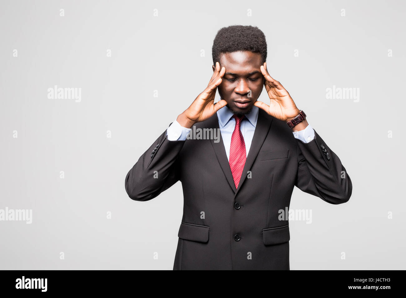 Sentirsi arrabbiato. Giovane africano nel convenzionale di toccare la sua testa con le mani e piedi contro lo sfondo grigio Foto Stock