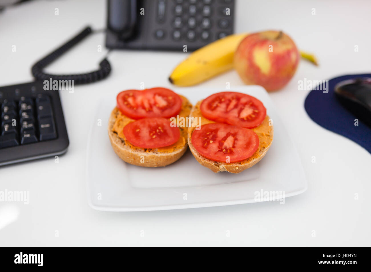 Mangiare sano al lavoro, sandwich con humus e pomodoro, mela e banana in background Foto Stock