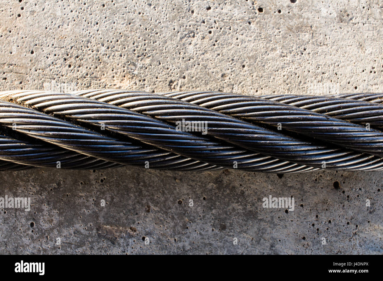 Twisted fune di acciaio sul grigio di una soletta in calcestruzzo. Foto Stock