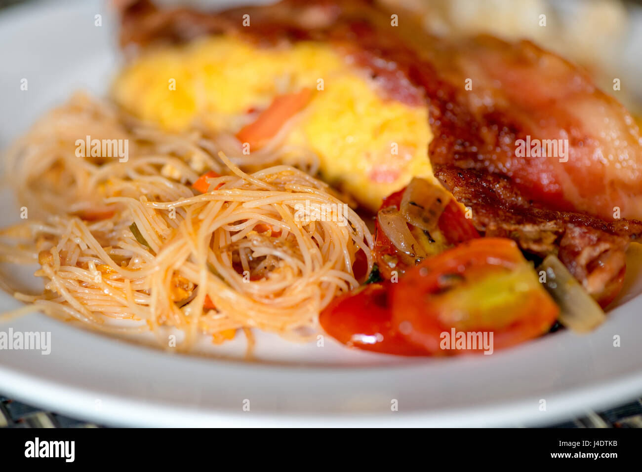 Piatto asiatico - noodles fritti con uova, pomodori e pancetta close-up su una piastra Foto Stock