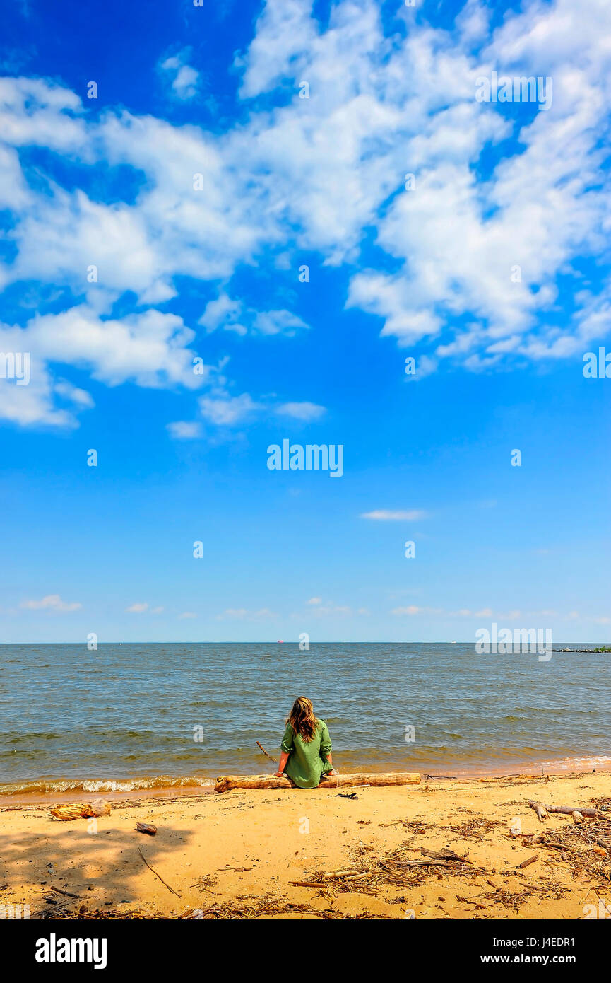 Una ragazza gode di un giorno di estate in spiaggia seduto su un log alla ricerca fino al cielo Foto Stock