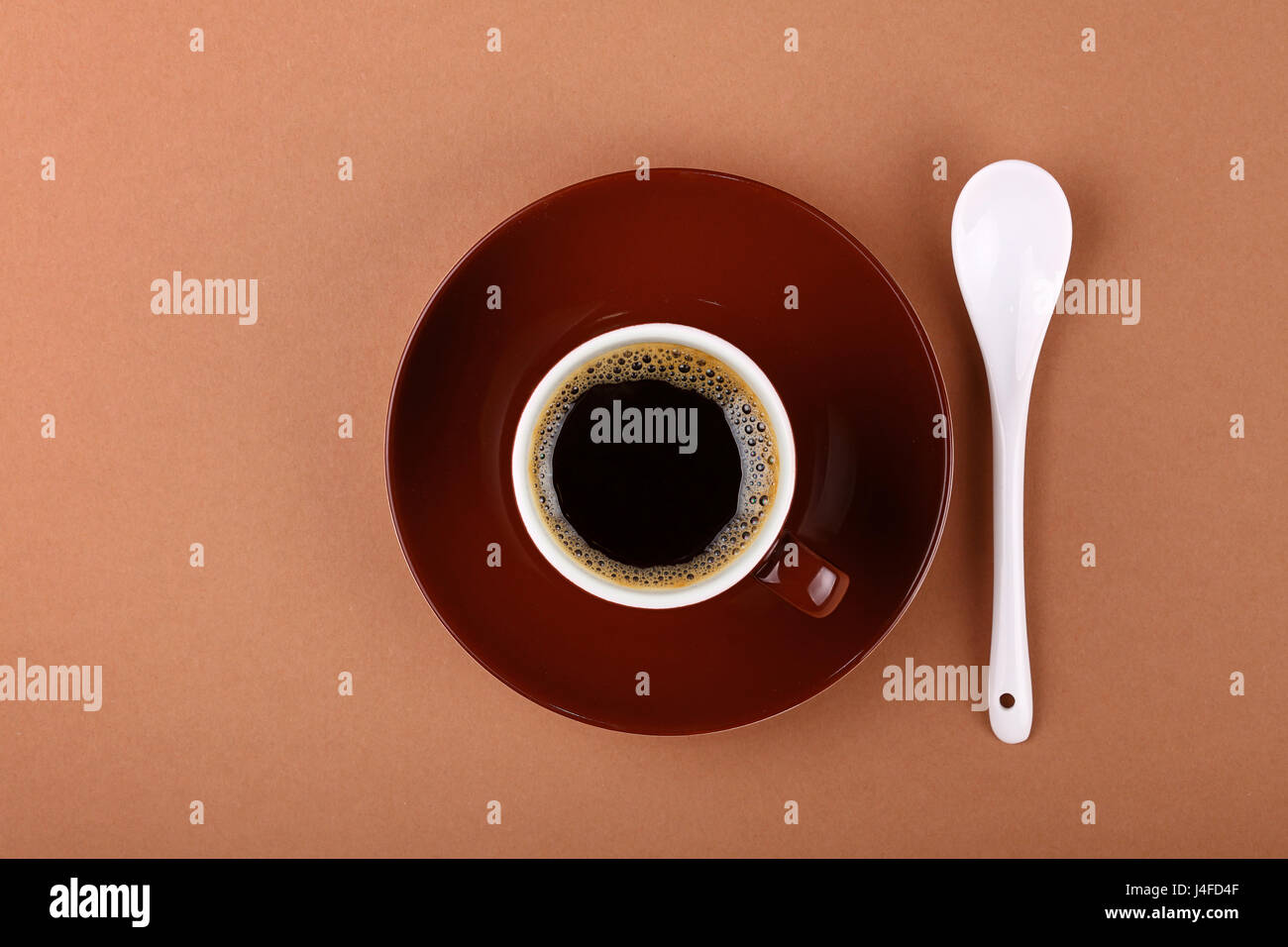 Piena di piccole dimensioni in ceramica marrone tazzina di caffè nero con piattino e cucchiaino di colore bianco su carta pergamena, close up, elevati vista dall'alto, direttamente al di sopra di Foto Stock