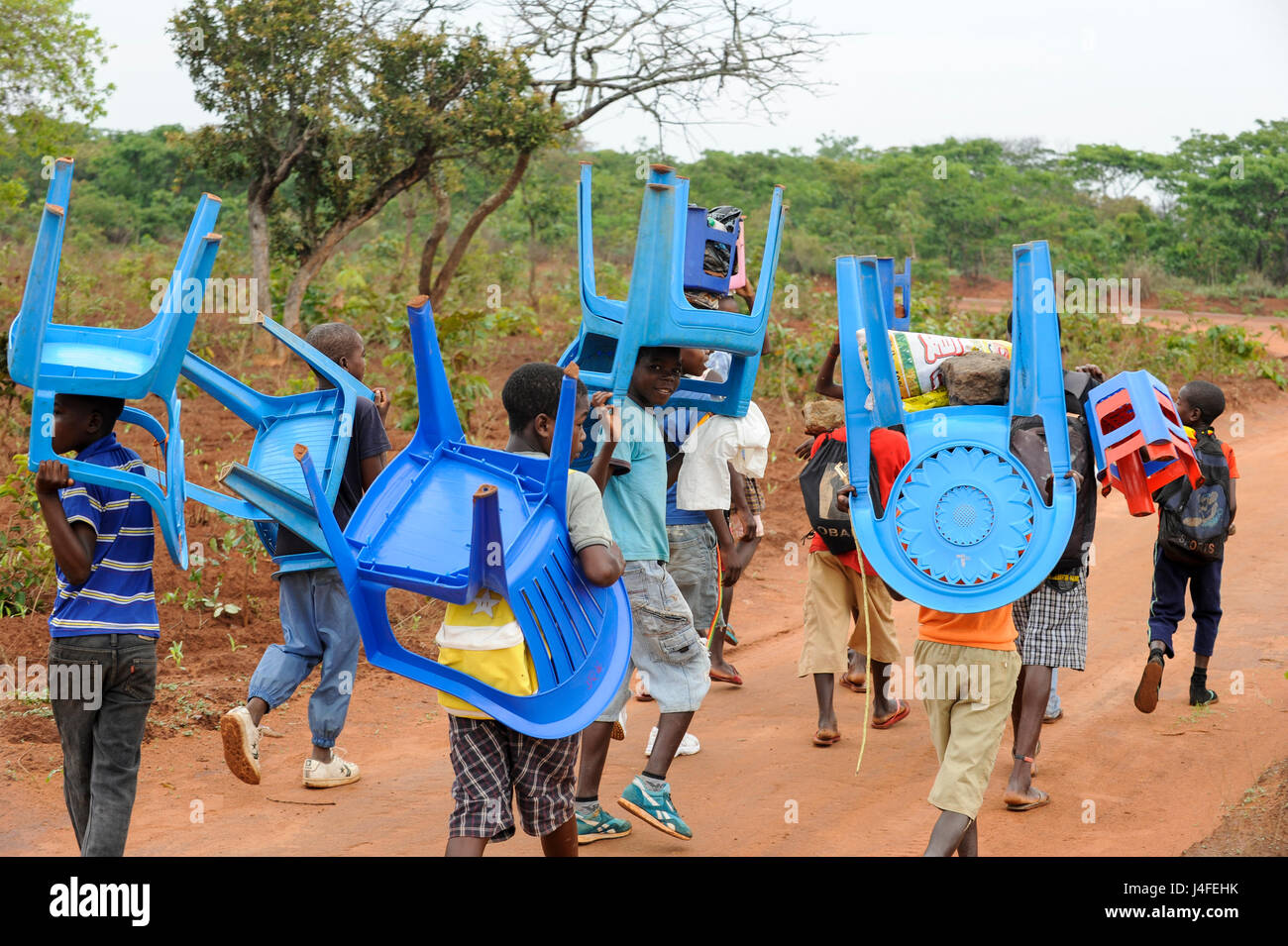 ANGOLA, Kwanza Sul, villaggio Kassombo, i bambini sulla strada per la scuola, ogni bambino deve portare la propria sedia in plastica come le scuole in cattivo stato a causa della guerra civile e la corruzione, i ricavi da olio ricco Angola sembra non raggiungere i villaggi / ANGOLA Kwanza Sul, Dorf Kassombo, Kinder mit Plastikstuehlen auf dem Weg zur Schule durch Felder des Dorfes, da die Schulen durch den Buergerkrieg zerstoert und ohne Inventar sind, muss jedes tipo seinen Plastik Stuhl mitbringen Foto Stock