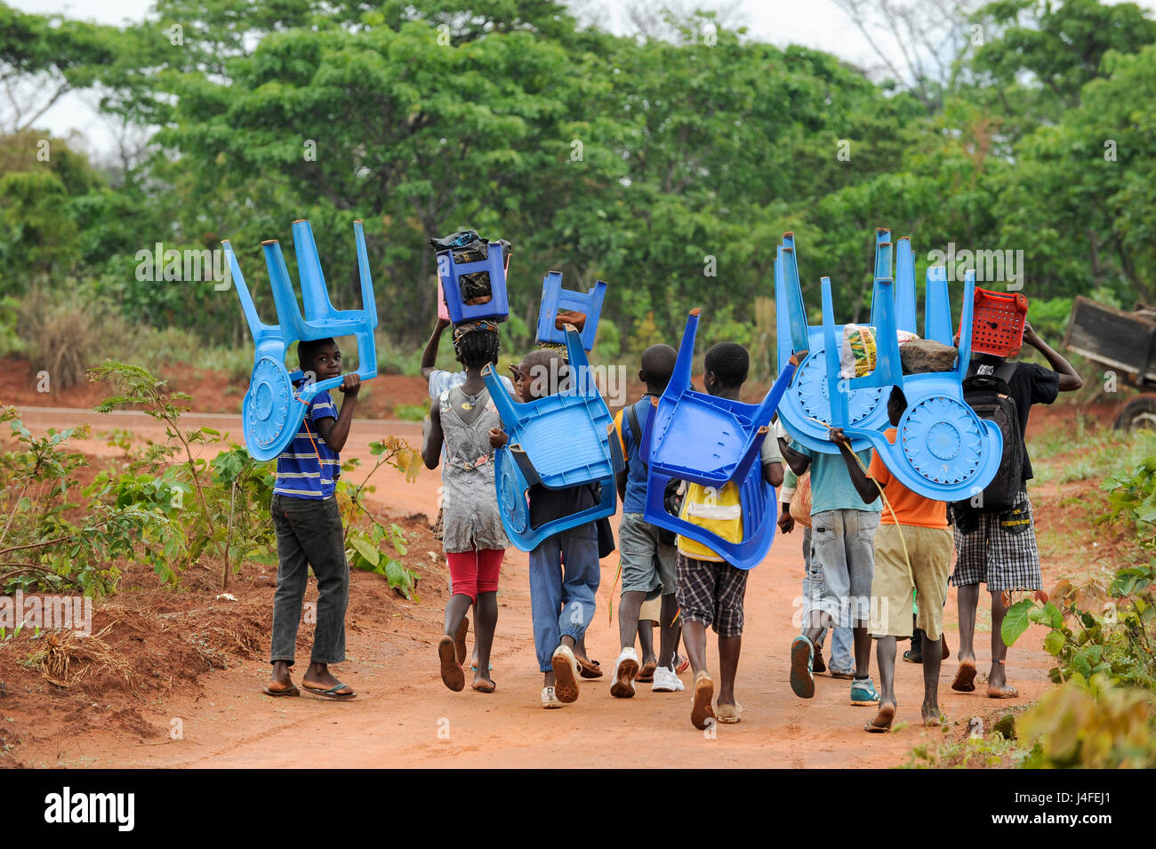 ANGOLA, Kwanza Sul, villaggio Kassombo, i bambini sulla strada per la scuola, ogni bambino deve portare la propria sedia in plastica come le scuole in cattivo stato a causa della guerra civile e la corruzione, i ricavi da olio ricco Angola sembra non raggiungere i villaggi / ANGOLA Kwanza Sul, Dorf Kassombo, Kinder mit Plastikstuehlen auf dem Weg zur Schule durch Felder des Dorfes, da die Schulen durch den Buergerkrieg zerstoert und ohne Inventar sind, muss jedes tipo seinen Plastik Stuhl mitbringen Foto Stock