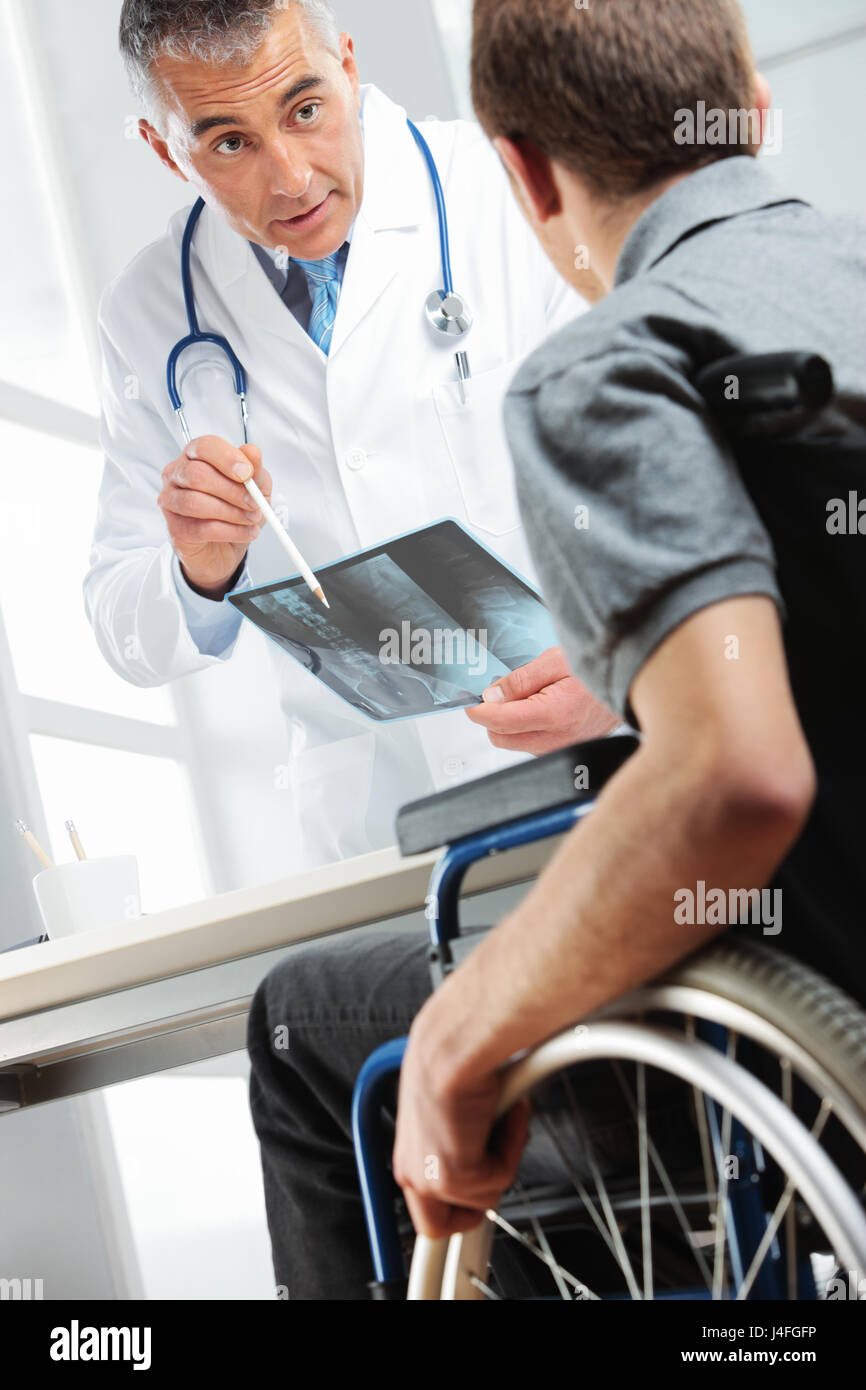 Giovane uomo su una sedia a rotelle incontro medico ortopedico. Essi sono in cerca di immagine a raggi x e consulenza circa la guarigione. Foto Stock