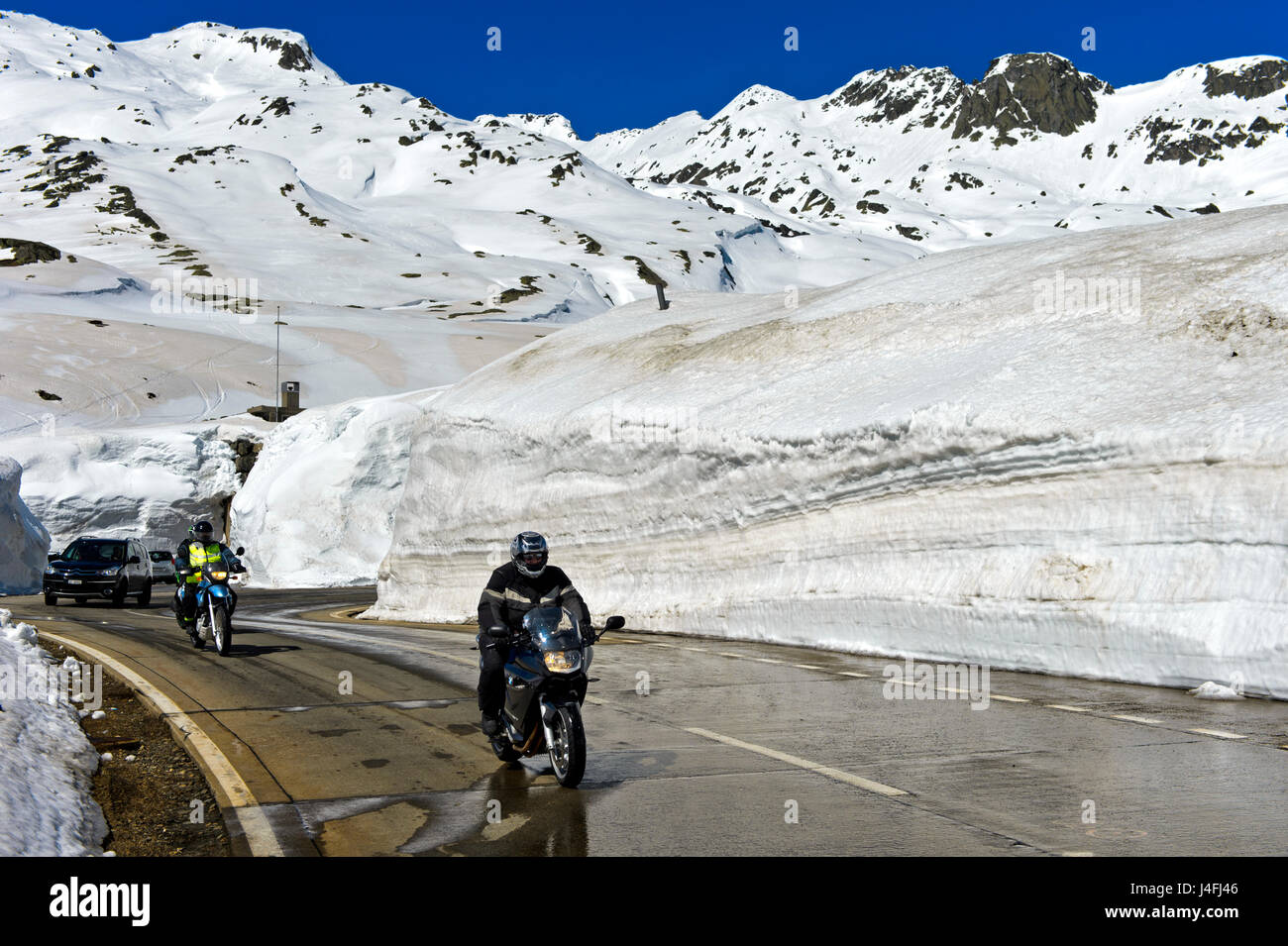 Due motociclisti che attraversa il San Gottardo sulla strada del passo tra alti muri di neve, San Gottardo, Canton Ticino, Svizzera Foto Stock