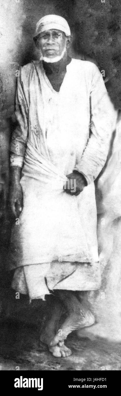 Questa immagine raffigura Shirdi Sai Baba, un venerato santo indiano, in piedi vicino a un muro. La scena cattura probabilmente la presenza spirituale di Sai Baba, una figura influente nella storia religiosa indiana. Foto Stock