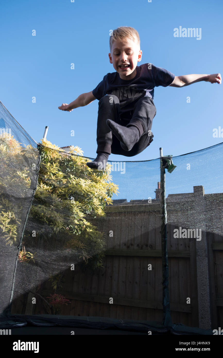 Ragazzo giovane avendo divertimento rimbalza su un trampolino nel suo giardino Foto Stock