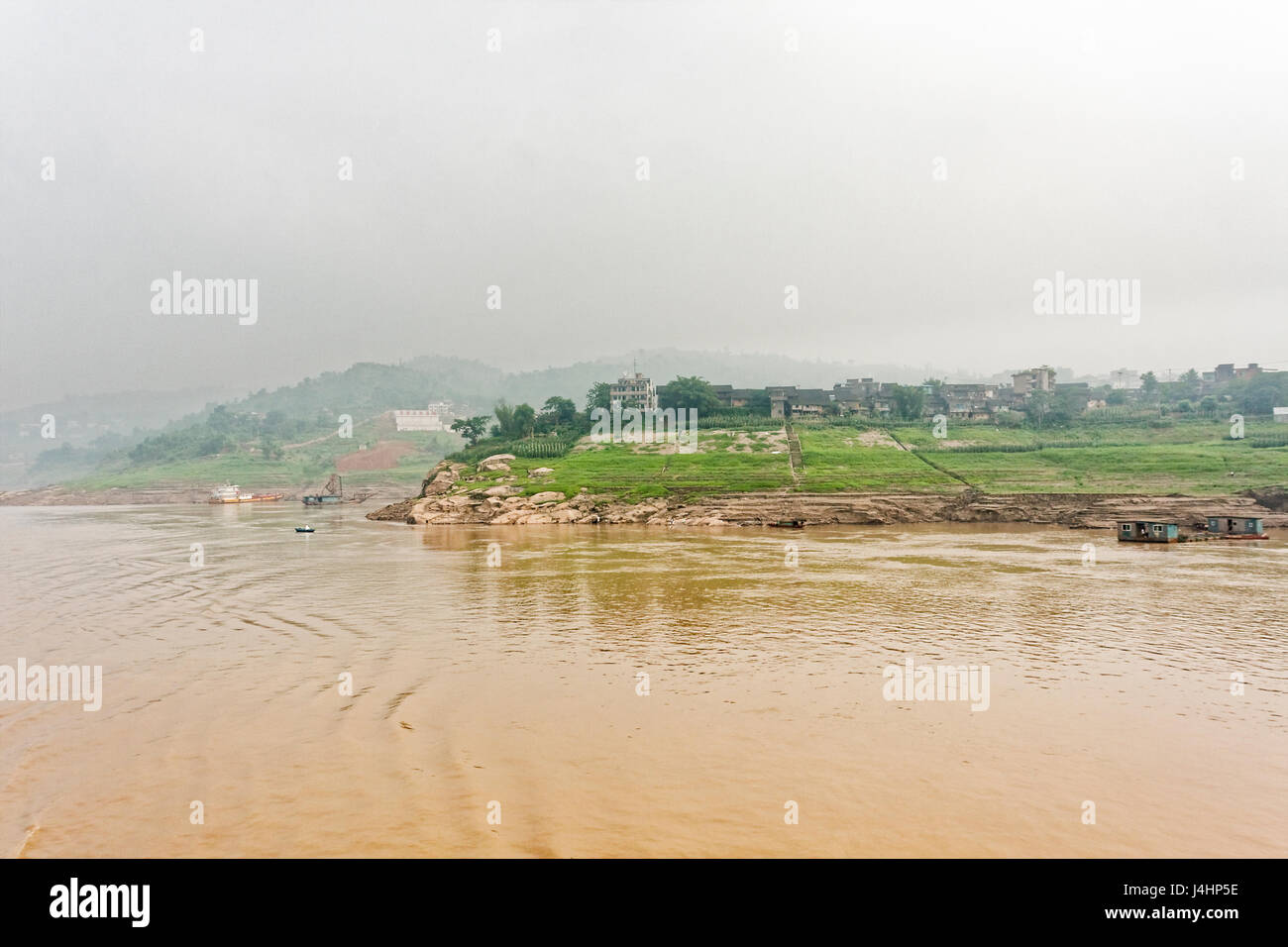 Case galleggianti ormeggiate sulle ripide sponde del fiume Yangtze, nei pressi di una piccola città sul fiume. La nebbia si raccoglie nelle lontane colline. Foto Stock