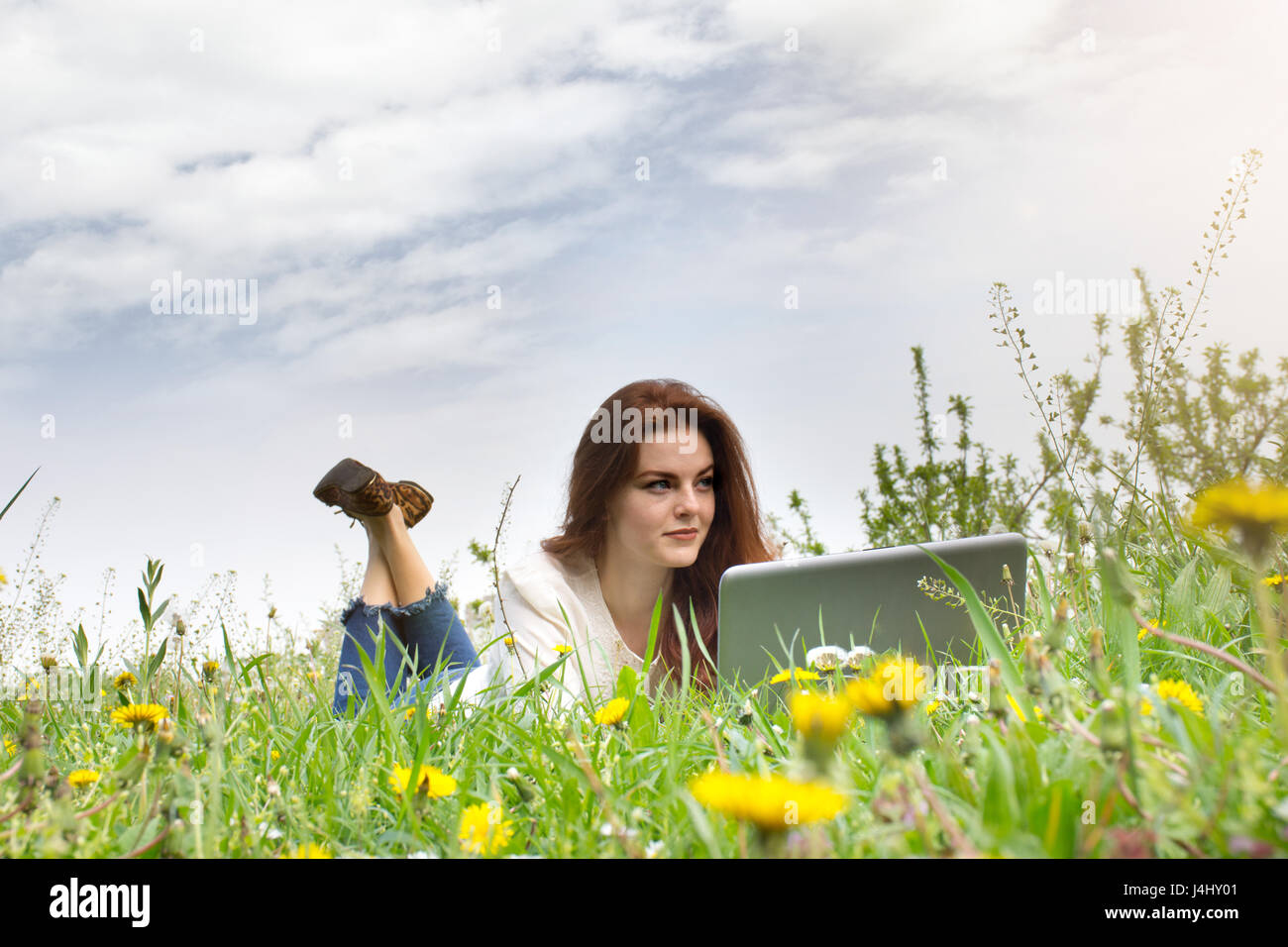 Redhead donna utilizzando laptop nel parco sdraiati sull'erba verde. Foto Stock