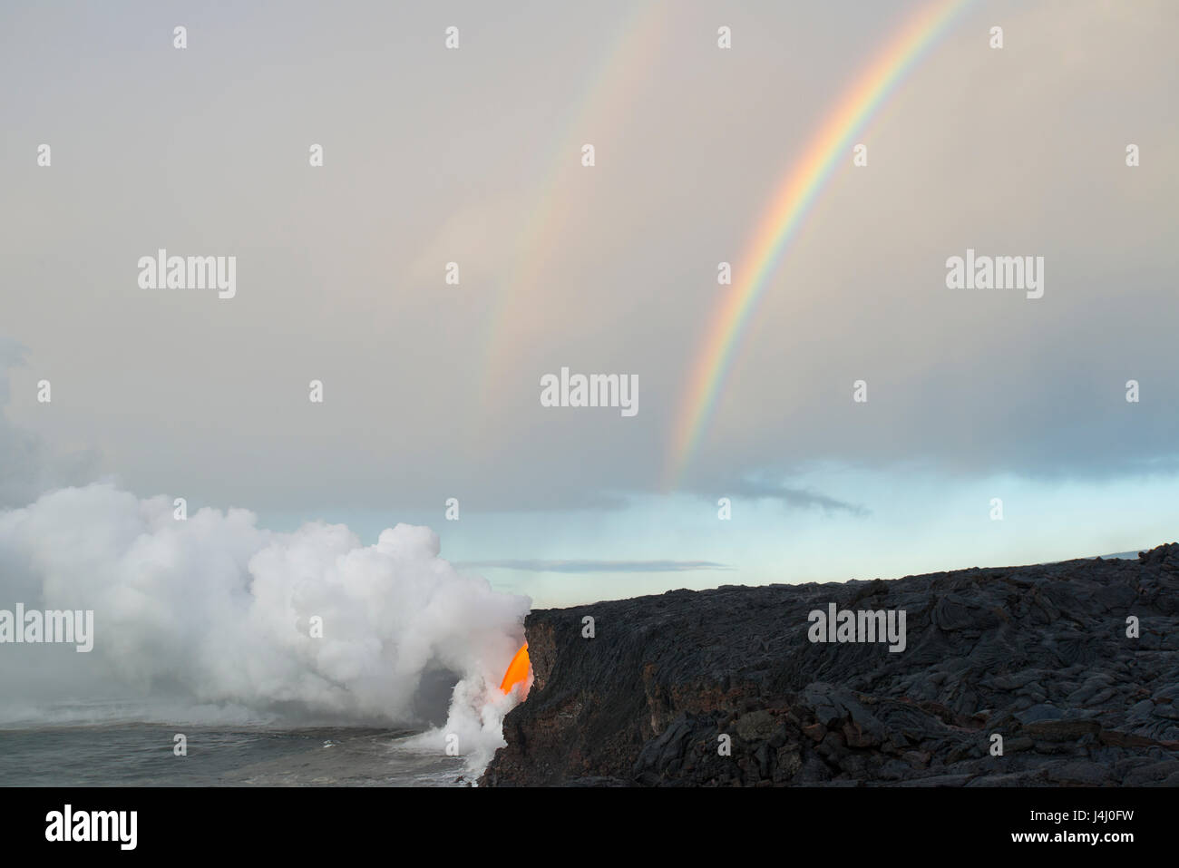 Un doppio arcobaleno tocca verso il basso dove hot lava dal vulcano Kilauea entra nell'oceano dalla estremità aperta di un tubo di lava a Kamokuna, Isola delle Hawaii, STATI UNITI D'AMERICA Foto Stock