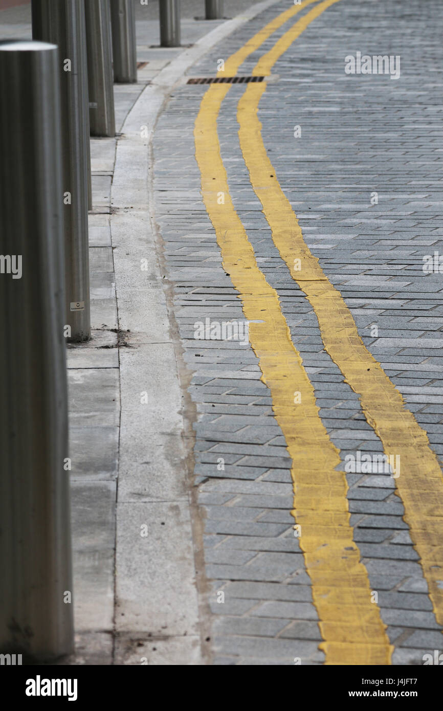 Doppio giallo linee sulla strada di mattoni con bitte Foto Stock