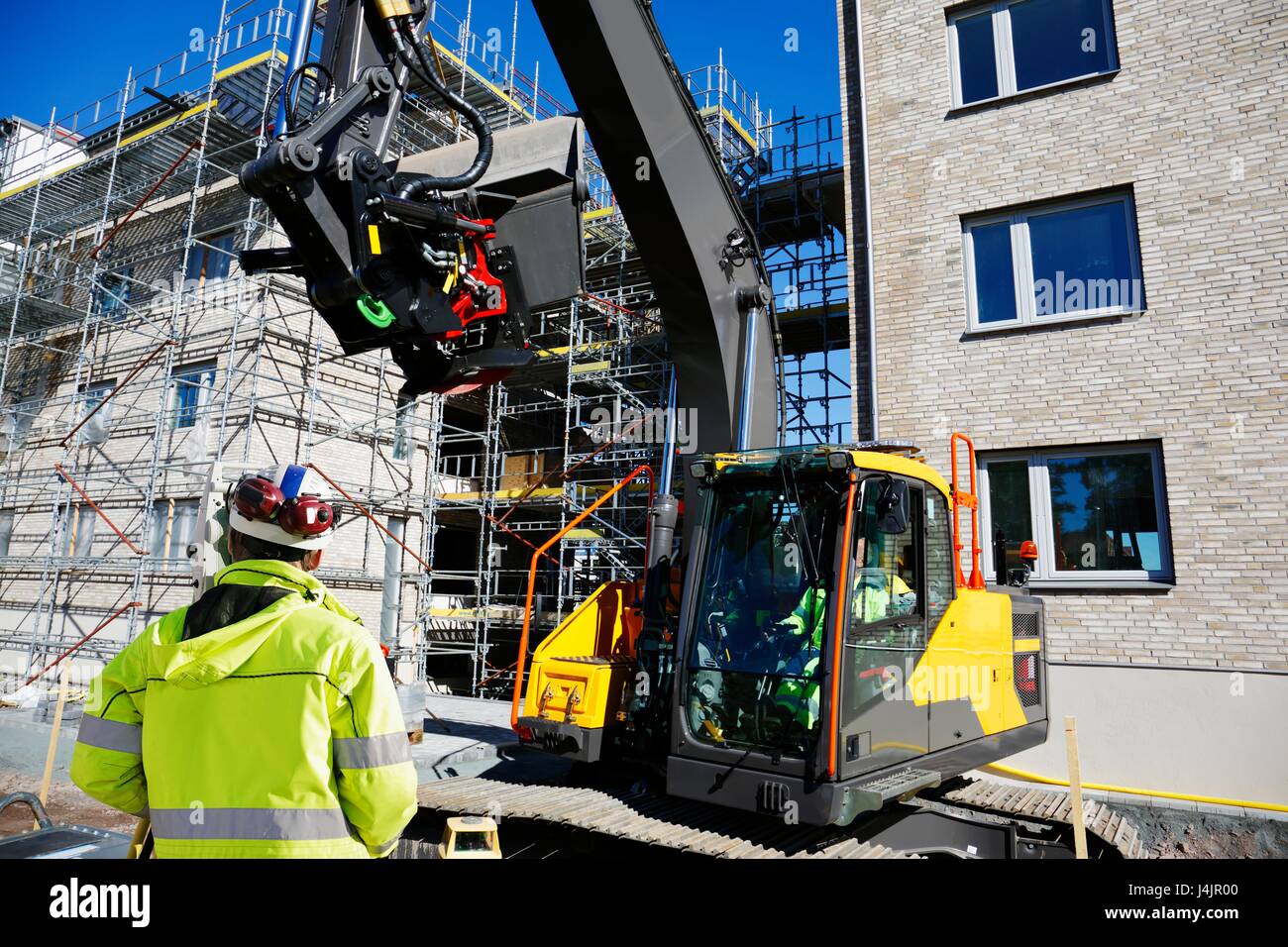 Operaio edile sul sito con scavatrice. Foto Stock