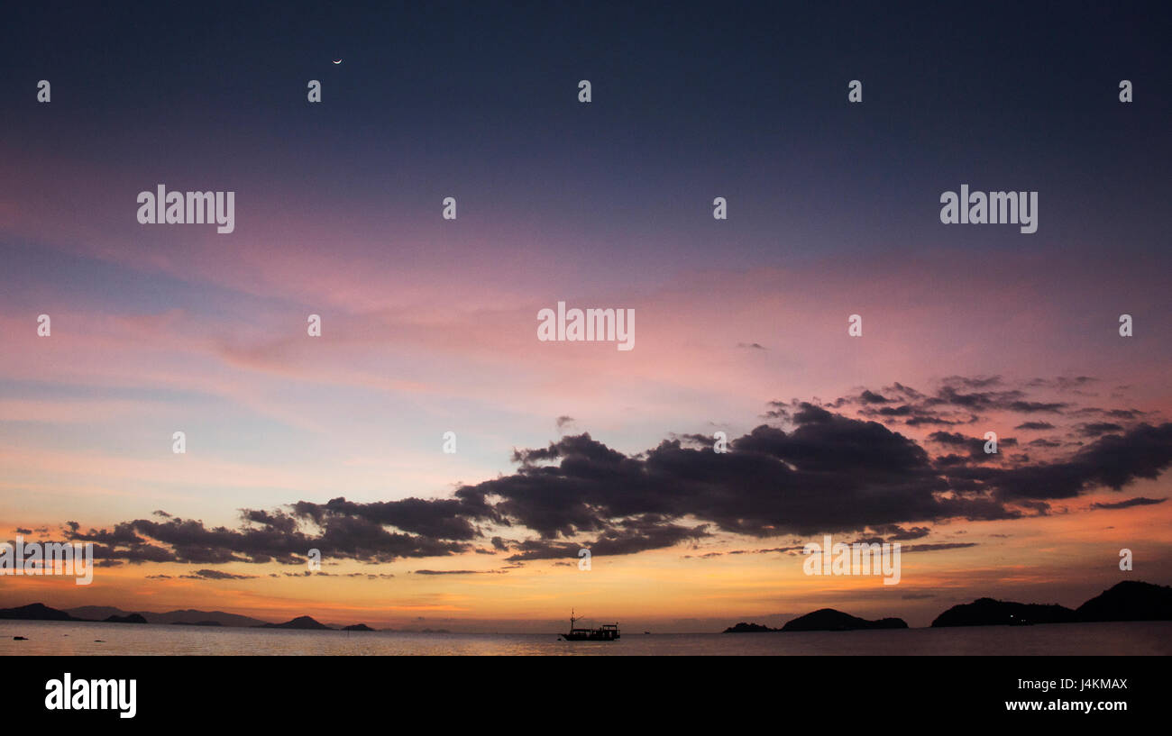 Silhouette di barca di attraversare l'oceano al tramonto con orange viola porpora di colore blu Cielo di tramonto sull'orizzonte, Labuan Bajo Bajawa. Foto Stock