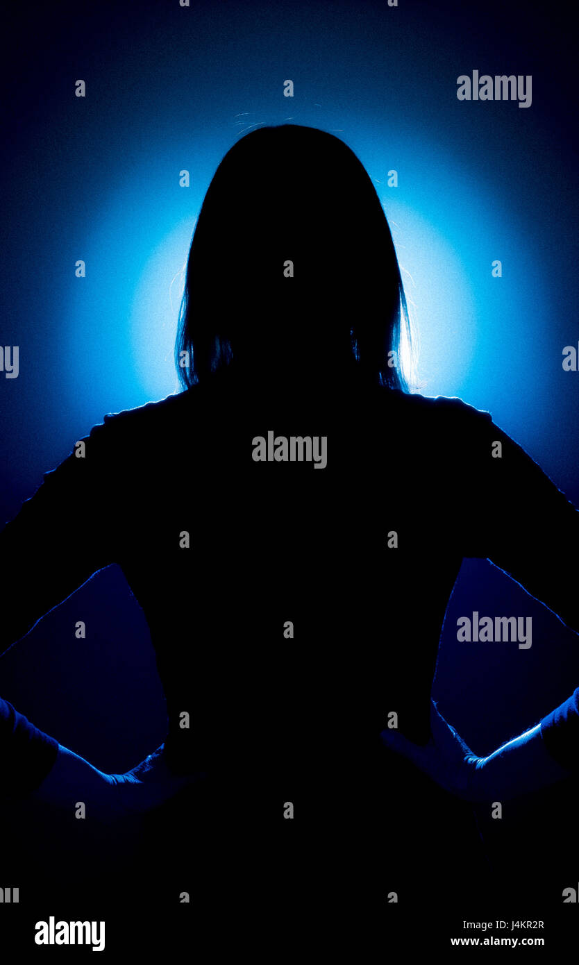 Silhouette di donna con torna alla fotocamera e le mani sui fianchi contro la macchia blu sullo sfondo illuminato Foto Stock