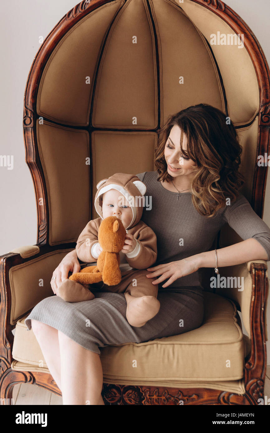 Madre caucasica seduto in poltrona con baby figlio indossando il costume orso Foto Stock