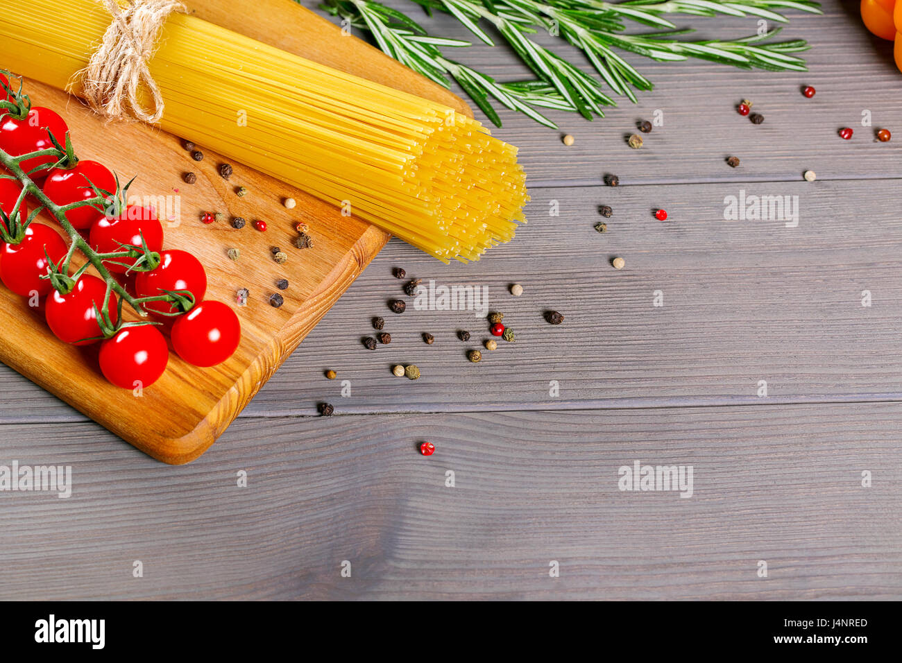 Spaghetti, pomodori ciliegia, olio d'oliva e spezie sul vecchio grigio Sfondo di legno Foto Stock