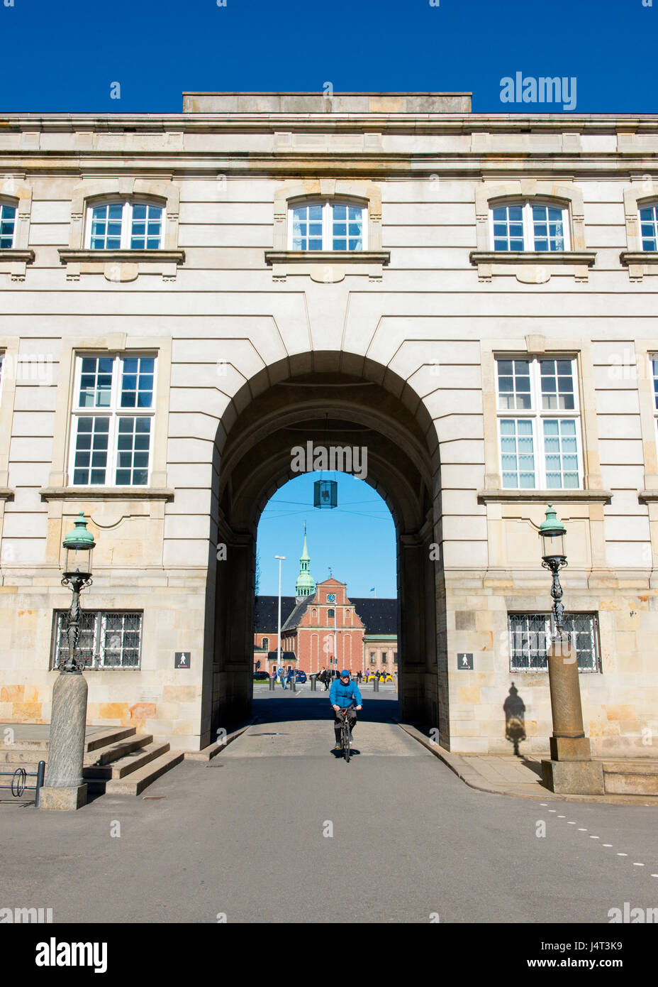 Ciclista pedalando attraverso archway di Christiansborg Slot, con vista della chiesa di Holmen in background. Copenaghen, Danimarca Foto Stock