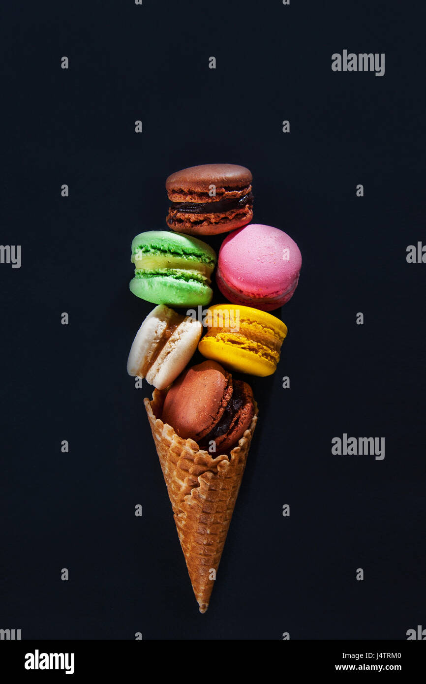 Torta multicolore macaron o amaretto nel cono di cialda nella forma di gelati su sfondo nero. Vista dall'alto. Foto Stock
