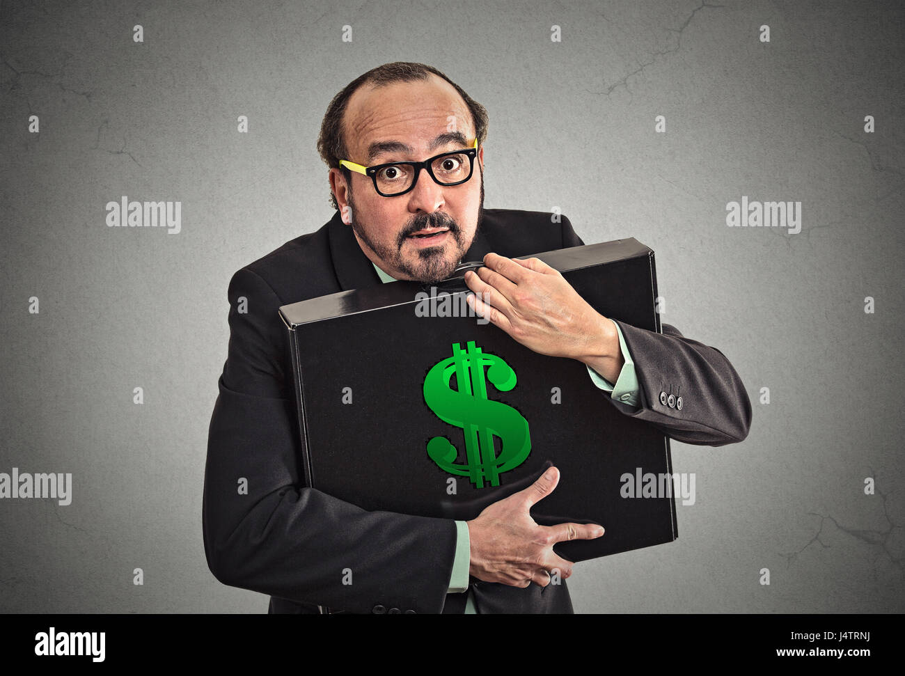 L'avidità di denaro. Business man azienda azienda caso con dollari isolato a tenuta sulla parete grigia sullo sfondo. Culto, avaro, eccessivo guadagno, concetto di finanza Foto Stock