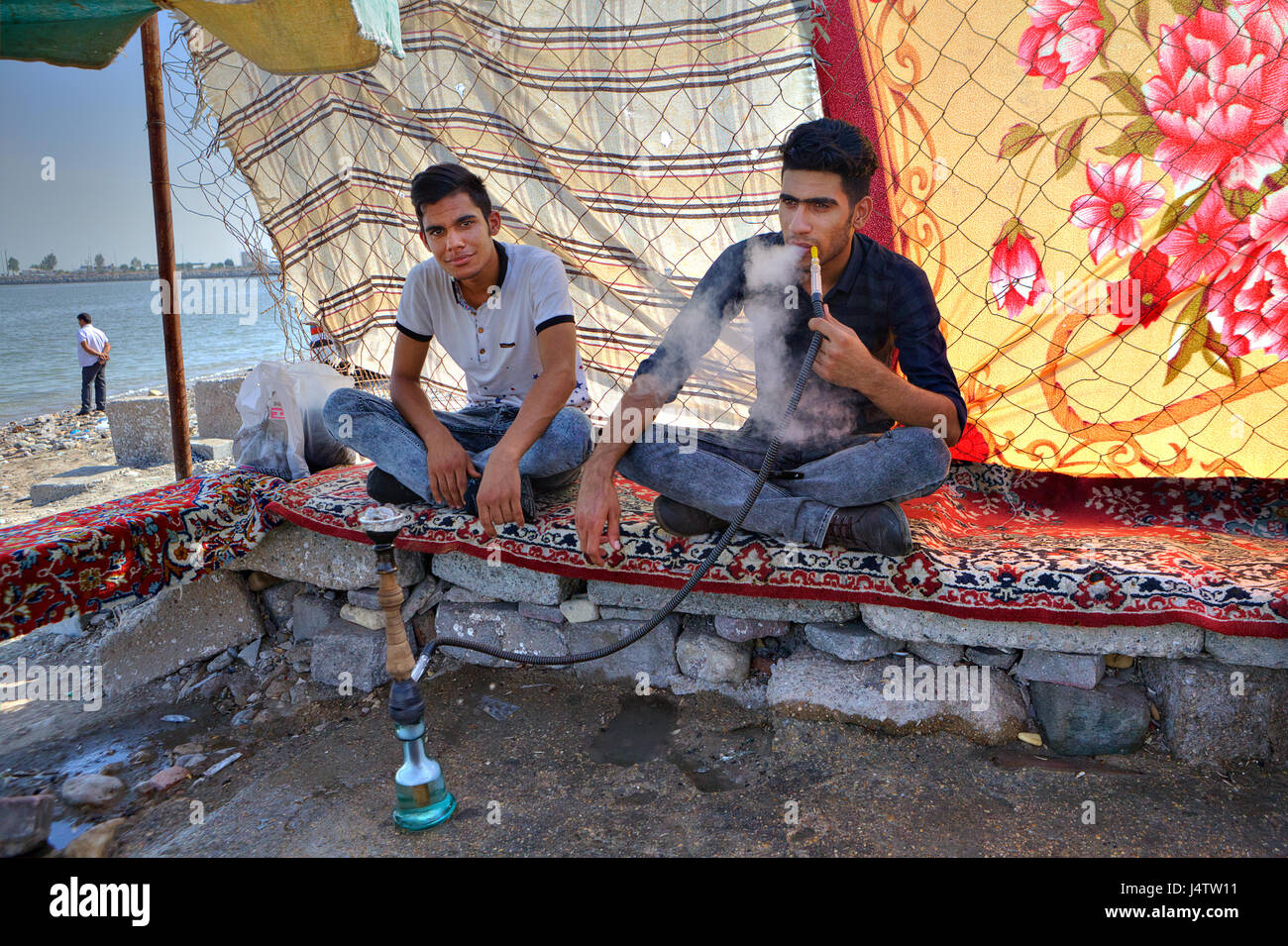 Bandar Abbas, Hormozgan Provincia, Iran - 16 aprile, 2017: due giovani uomini riposare all'ombra sotto la tettoia di stoffa, sulle rive del Golfo Persico e Foto Stock