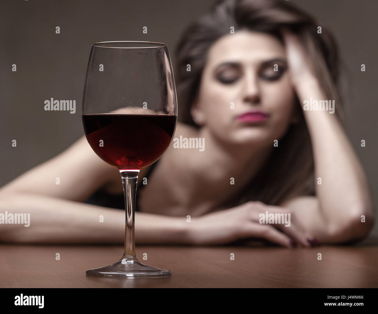 Giovane bella donna in depressione, bere alcool su sfondo scuro. Focus sul vetro Foto Stock