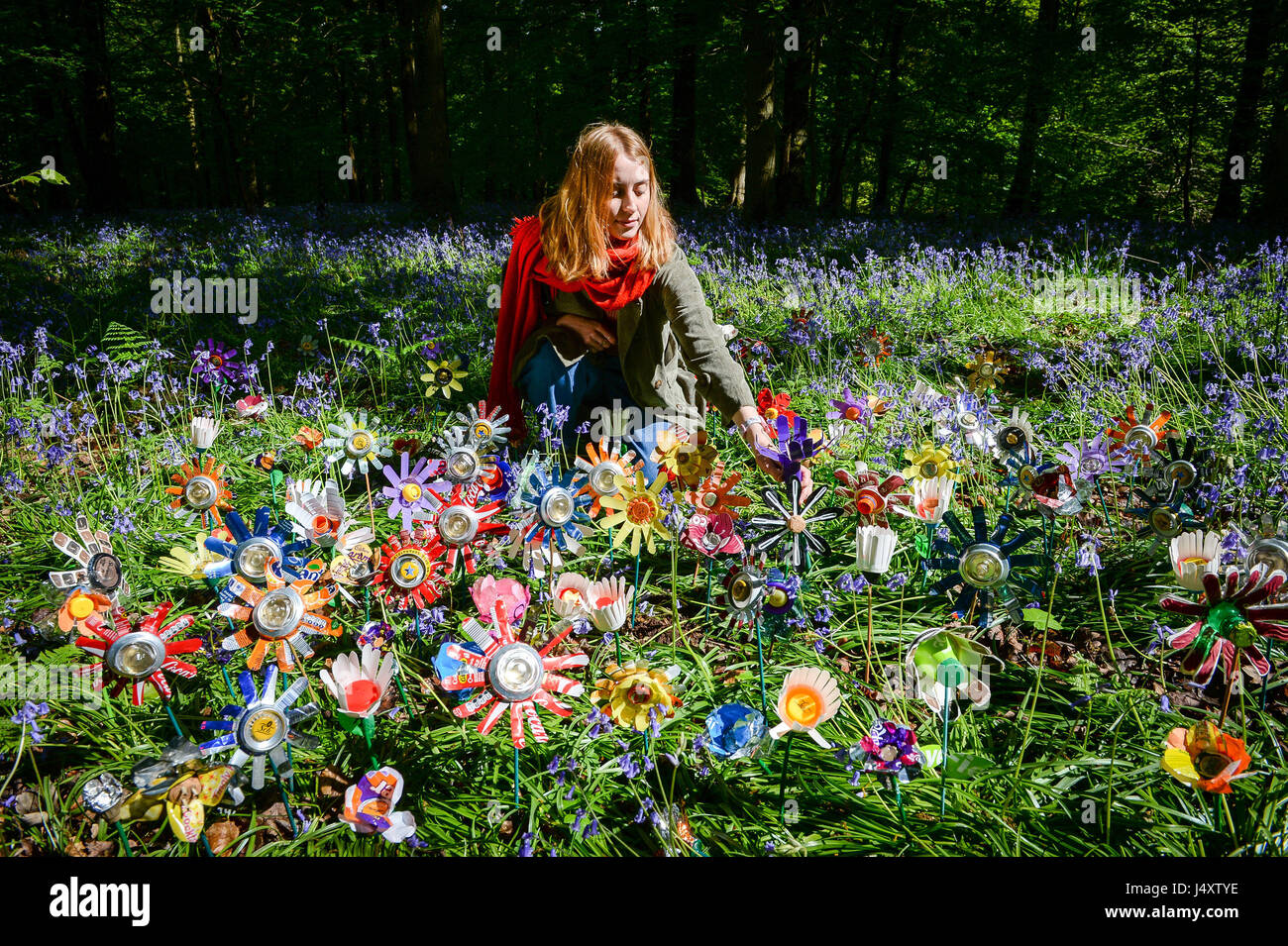 Il designer Lottie Hanson-Lowe organizza fiori fatti con lettiera riciclata dall'artista Michelle Reader, si trova tra le decine piantate sul pavimento della foresta come parte di un'installazione d'arte nella foresta di Dean, Gloucestershire, per aumentare la consapevolezza dei problemi di lettiera rurale nella zona. Foto Stock