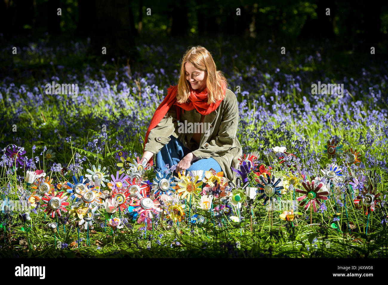 Il designer Lottie Hanson-Lowe organizza fiori fatti con lettiera riciclata dall'artista Michelle Reader, si trova tra le decine piantate sul pavimento della foresta come parte di un'installazione d'arte nella foresta di Dean, Gloucestershire, per aumentare la consapevolezza dei problemi di lettiera rurale nella zona. Foto Stock