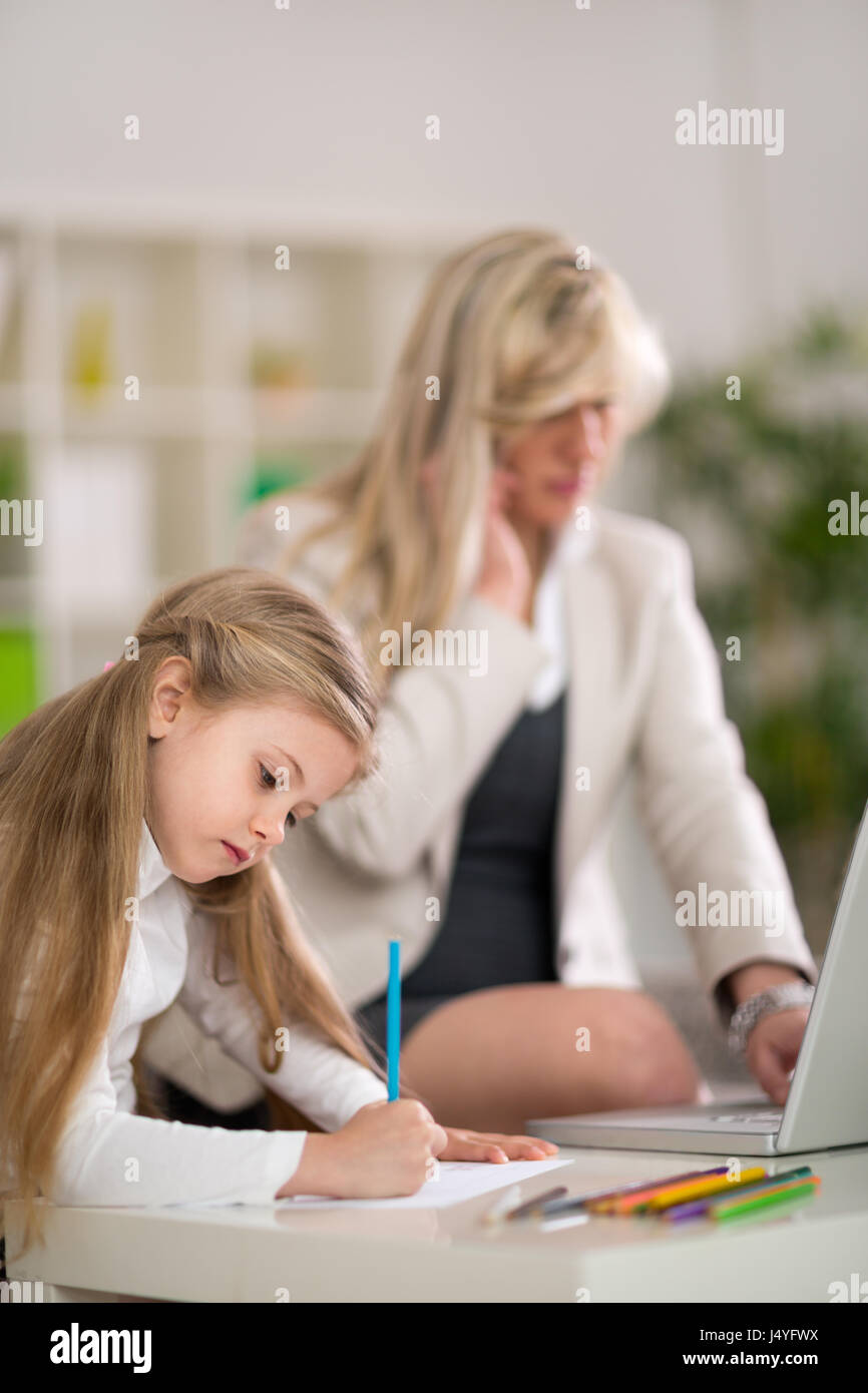 La mamma e imprenditrice funziona con computer portatile a casa mentre la sua piccola figlia giocando Foto Stock